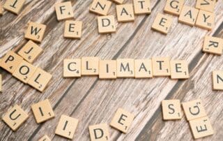 Wooden Scrabble tiles arranged to spell 'CLIMATE' on a wooden surface.